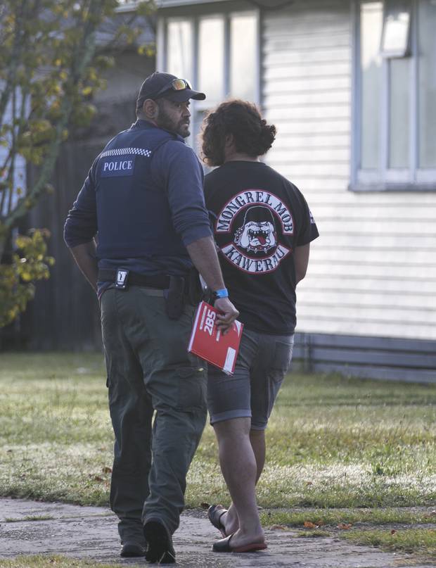 A Mongrel Mob gang member is led away after police raided the gang's headquarters in Kawerau. 