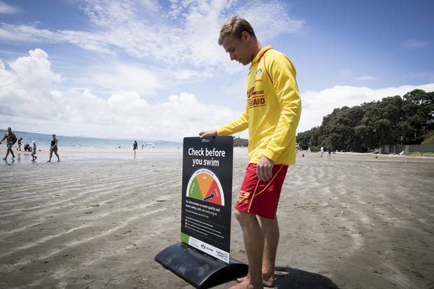 Lifeguard Dan Lee stands with a sign at Takapuna Beach warning people of the water quality on the beach. Photo / Dean Purcell