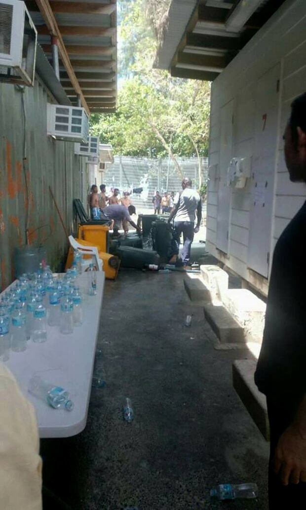 Refugees and asylum seekers watch as immigration officials empty water tanks and turn over the water bins being used to collect the rain water. Photo / AP