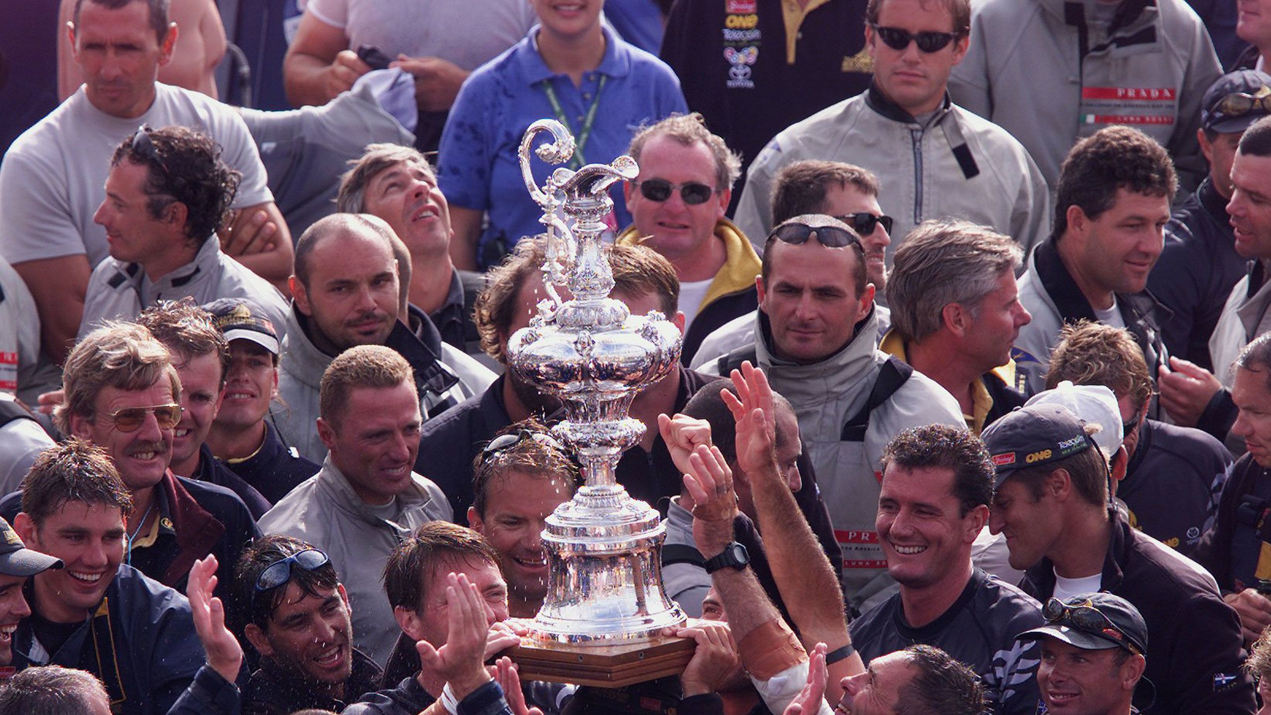 Prada team members look on as Team NZ crew celebrate their win at the 2000 America's Cup at the Viaduct Basin. New Zealand Herald Photograph by Mark Mitchell.