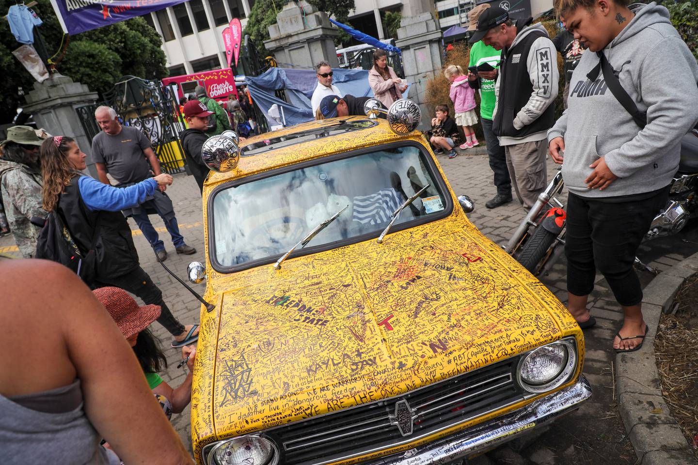 一辆黄色迷你车停在议会场地上，上面写满了抗议者写的信息。 照片/迈克·斯科特
