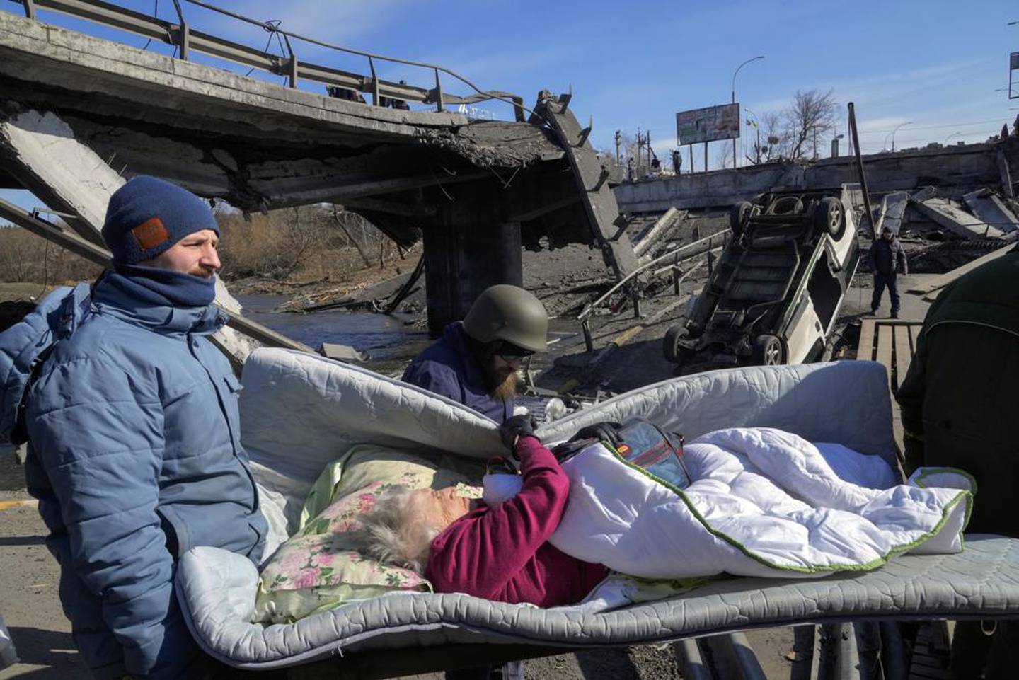 基辅西北部 Irpin 的志愿者在疏散一名老年居民时，在一座被毁坏的桥下经过一条临时小路。 照片/美联社