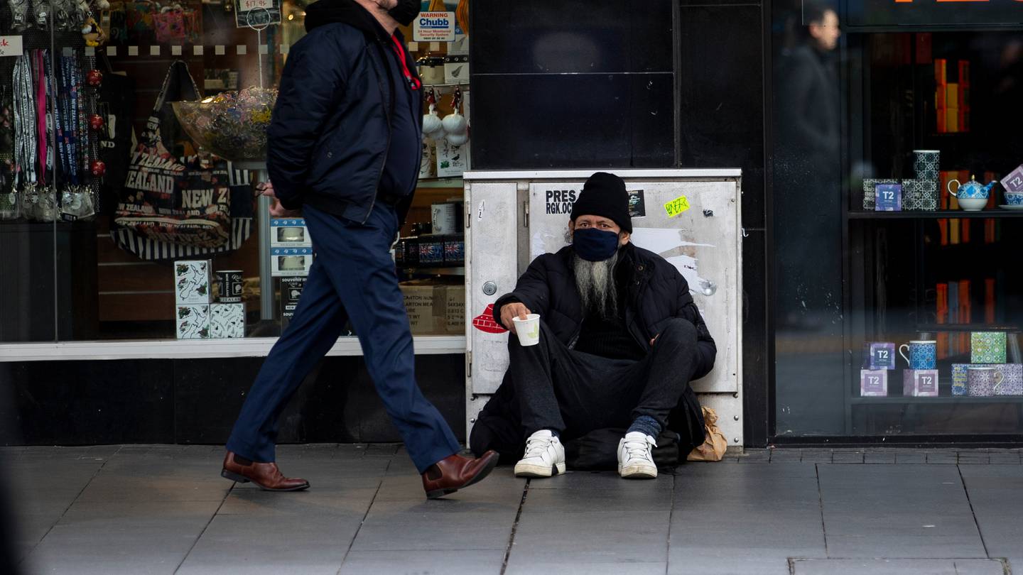 A pedestrian on Auckland's Queen St walks past a rough sleeper, holding up a discarded coffee cup for charity. Photo / Dean Purcell, File