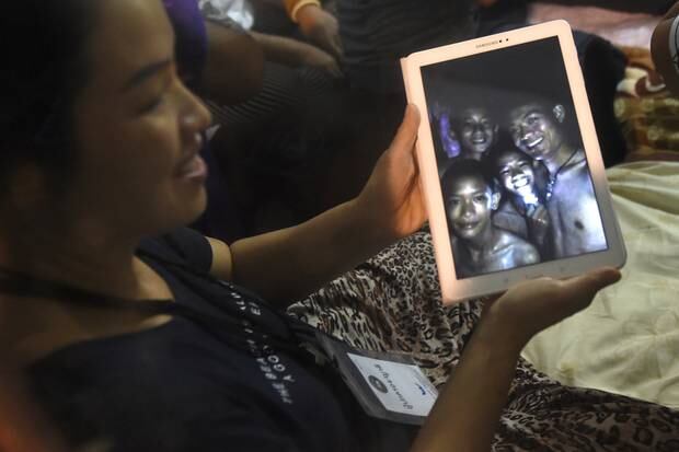 A happy family member shows the latest pictures of the missing boys taken by rescue divers. Photo / AP