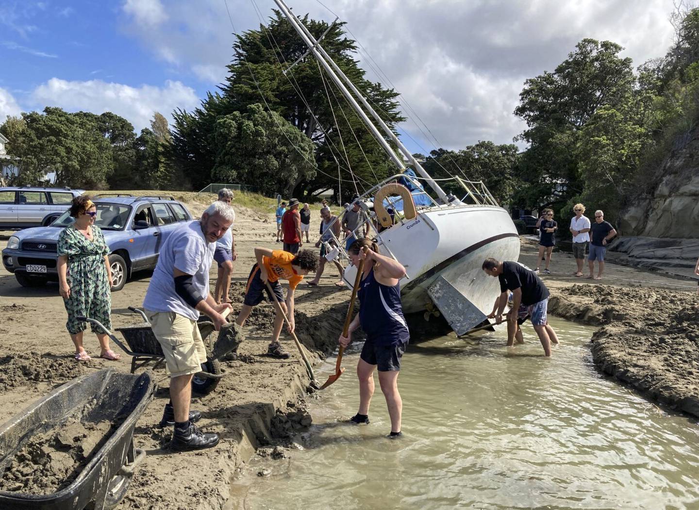 Manly Beach locals dig a channel to try to refloat a yacht washed up by Cyclone Dovi. Photo / Neville Marriner