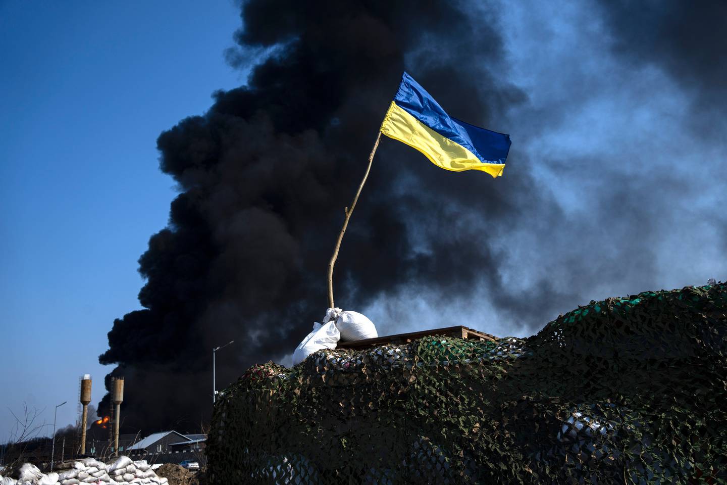 3 月 25 日，在俄罗斯发动袭击后，乌克兰军队在基辅郊区的燃料库中冒出黑烟，在检查站的顶部可以看到一面乌克兰国旗。照片/美联社