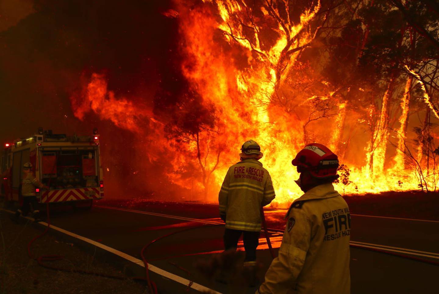 Fire and Rescue personal run to move their truck after a bushfire burns in extreme weather conditions next to a major road and homes on the outskirts of the town of Bilpin, NSW. Photo / Getty Images