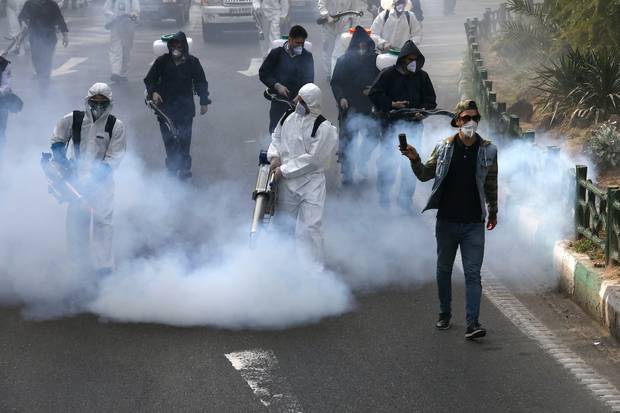 Firefighters disinfect a square against the new coronavirus as a man takes film, in western Tehran, Iran. Photo / AP