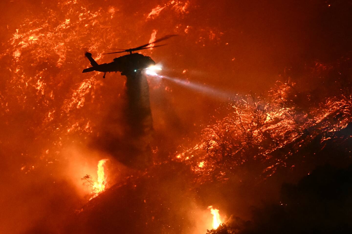 A fire-fighting helicopter drops water as the Palisades fire grows near the Mandeville Canyon on Saturday. Photo / Patrick T. Fallon, AFP