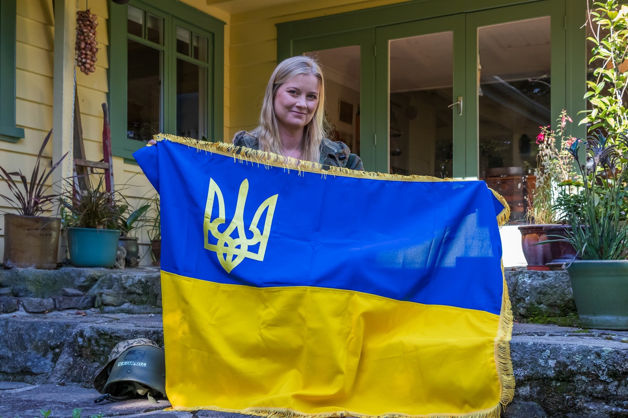  Harriet Campbell, known as &lsquo;Amy in Ukraine&rsquo; at home in Tauranga, with a Ukraine flag and her helmet. Photo / Kelly O&rsquo;Hara