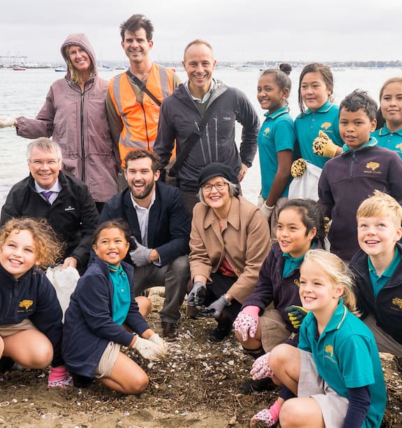 A group of volunteers, including children, collecting plastic toys and debris from a beach in Auckland. They are smiling and working together.