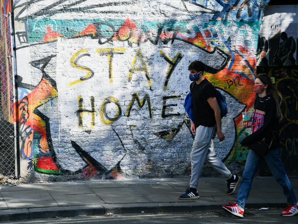 A couple wearing protective masks to protect against coronavirus walk past a mural reading 'Stay home', in the Shoreditch area, as the lockdown continues in London. Photo / AP