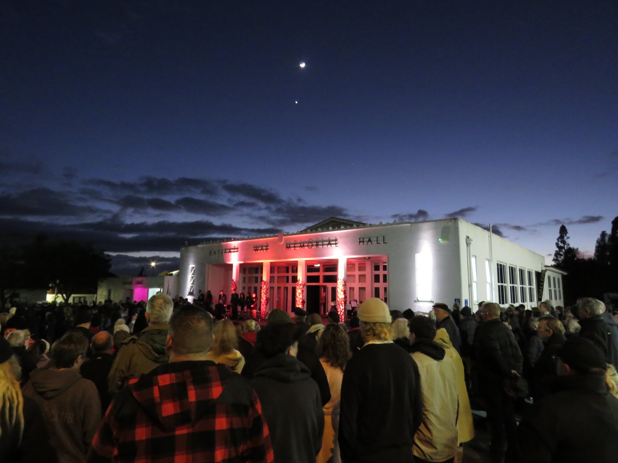  The crowd watches Katikati’s Anzac Day dawn at the War Memorial Hall service underneath a tiny moon and lone star in the sky. Photo / Merle Cave