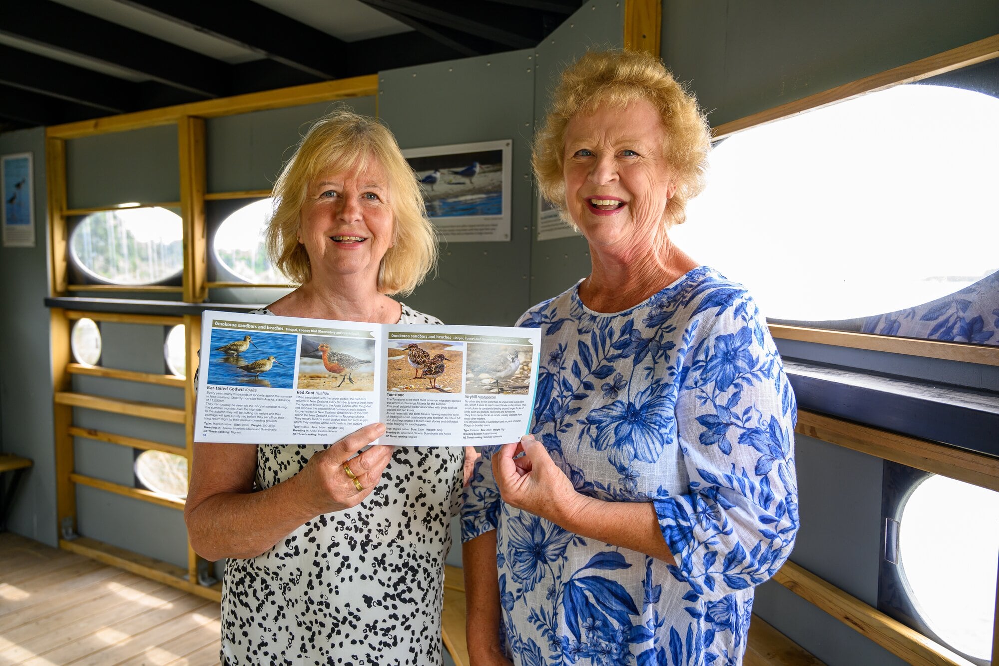 Sisters Evelyn Hiddinott and Christina Cleaver inside the bird observatory with the book Birds of Ōmokoroa. Photo / David Hall