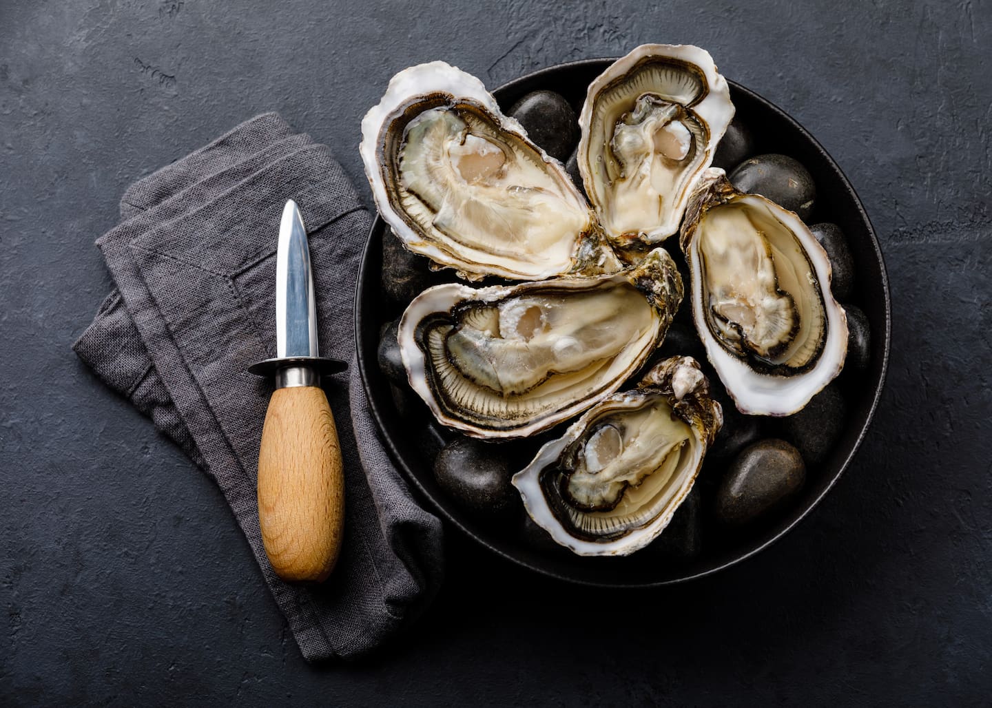 Fresh Bluff oysters with lemon and knife on stones on dark background. Photo / Getty Images