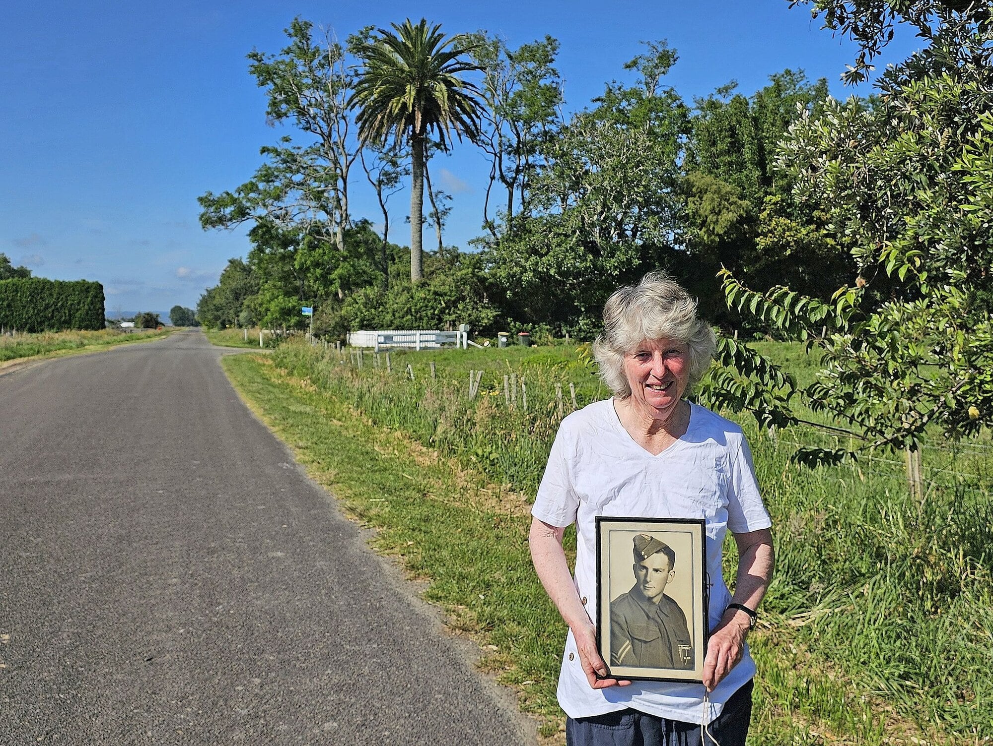 Robyn Askey with a photograph of her father, returned serviceman Laurie McLaren, who planted the phoenix palm in the background in 1950 when he was settled on the Putiki Road farm. Photo / Diane McCarthy