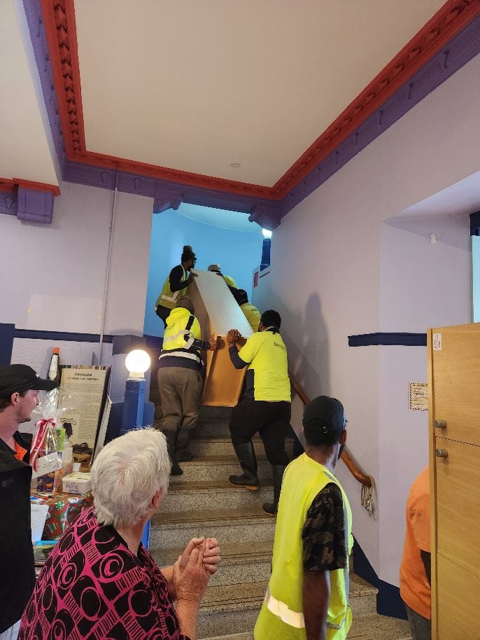 Recognised Seasonal Employer workers from Baygold carry donated kitchen furniture by Eastpack upstairs at the Te Puke Kiwifruit Heritage Hub on a rainy day.