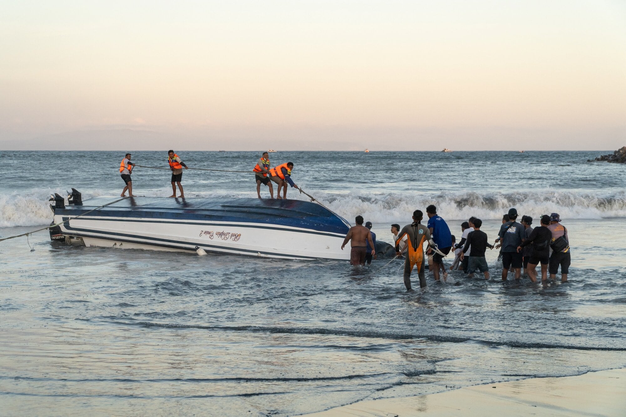 Locals and rescue workers attempt to recover an overturned speedboat after it sank near Sanur port in Bali on August 5, 2025. Three people were killed, including two Chinese nationals and an Indonesian crew member, after a boat sailing to the popular island of Bali with dozens onboard sank and ran aground, rescue authorities said. (Photo by Dicky Bisinglasi / AFP)