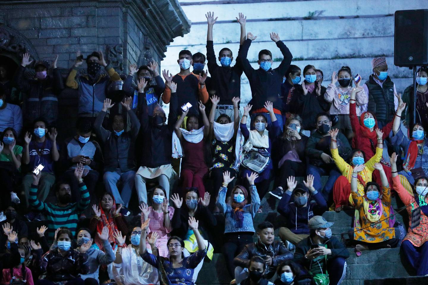 Nepalese people wearing face masks as a precaution against the coronavirus chant hymns as they gather for evening rituals at Pashupatinath Hindu temple in Kathmandu, Nepal. Photo / AP