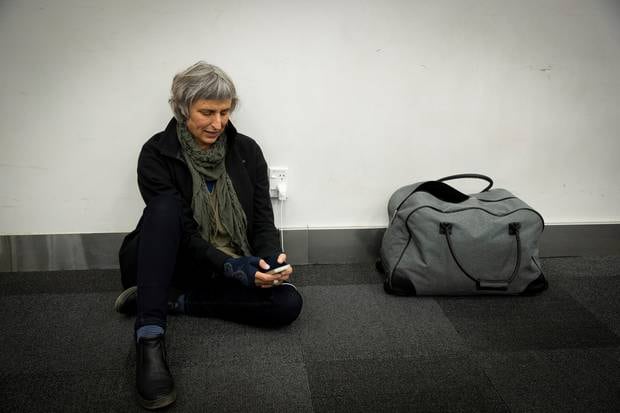Susan Lamont sits on the floor to charges her phone from a power point at Auckland Airport's domestic terminal. Photo / Dean Purcell